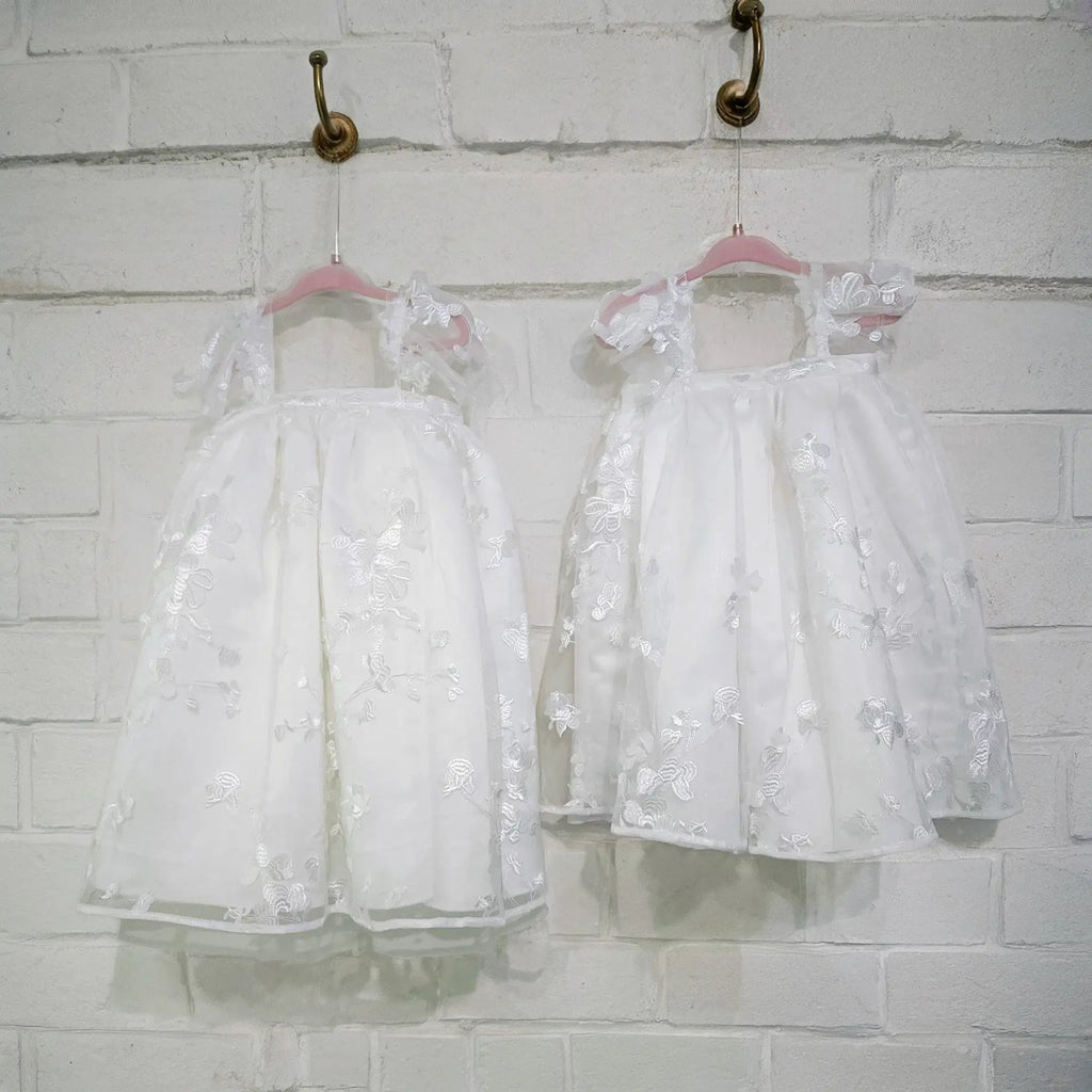 front view of two Babydoll Flower Girl Dresses with white brick background image 14