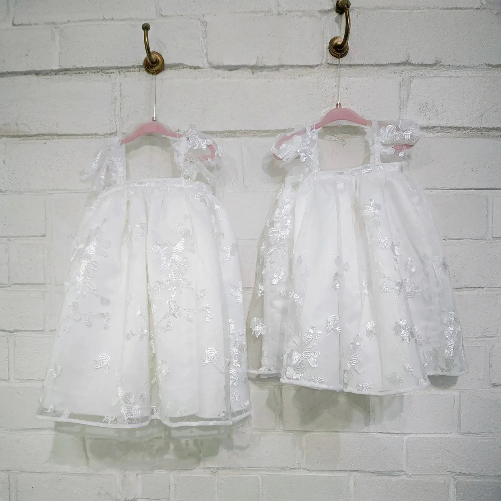 front view of two Babydoll Flower Girl Dresses with white brick background image 14